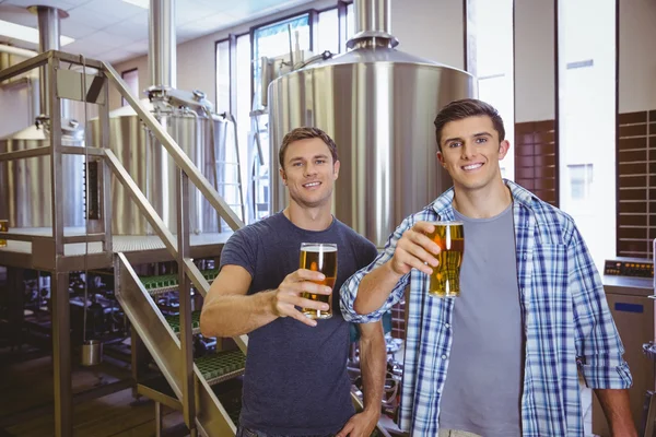 Jovens segurando uma caneca de cerveja sorrindo para a câmera — Fotografia de Stock