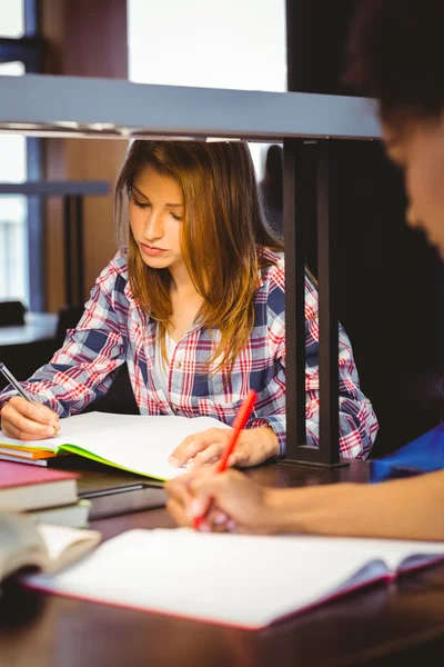 Studentin sitzt am Schreibtisch und schreibt in Notizblock — Stockfoto