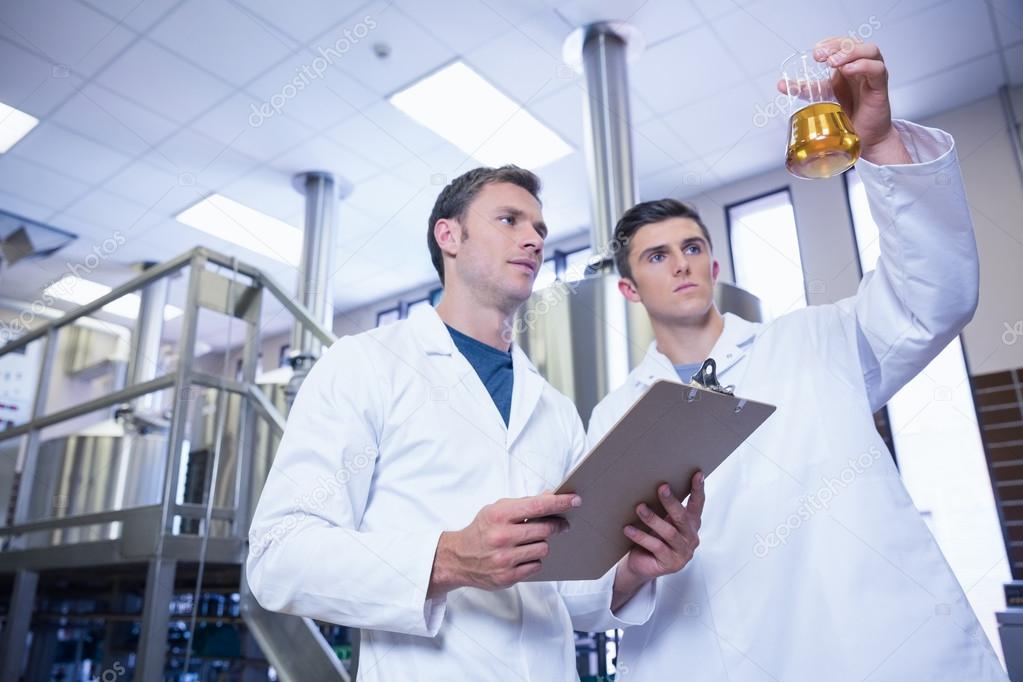 Two men in lab coat looking at the beaker with beer Stock Photo by