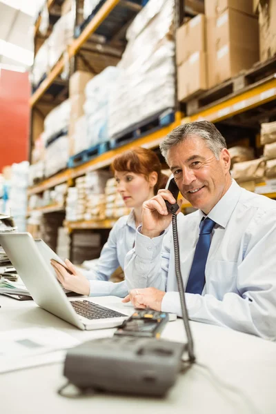 Manager working on laptop and talking on phone at desk — Stock Photo, Image