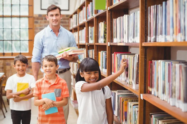 Симпатичные ученики и учитель ищут книги в библиотеке — стоковое фото