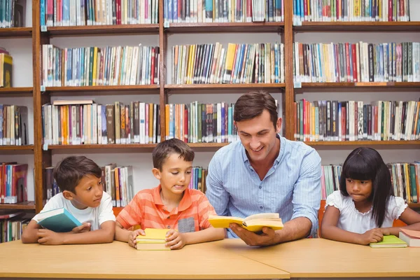 Lindos alumnos y profesor de lectura en la biblioteca —  Fotos de Stock