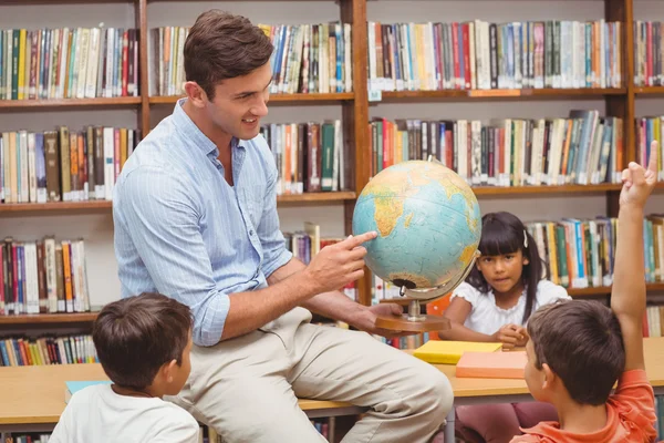 Cute pupils and teacher looking at globe in library — Stock Photo, Image