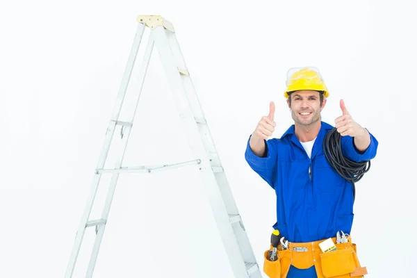 Electrician gesturing thumbs up by ladder — Stock Photo, Image
