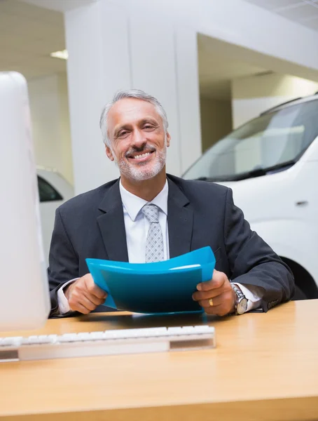 Un hombre de negocios sonriente sosteniendo una carpeta en su escritorio — Foto de Stock