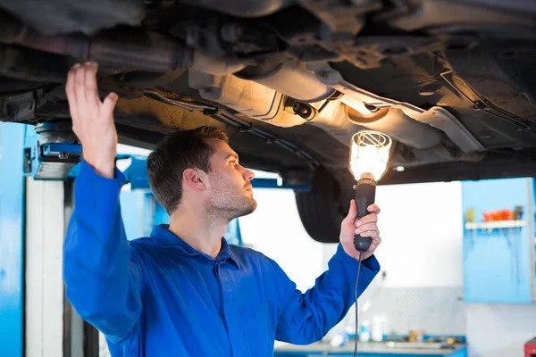 Mechaniker schaut mit Taschenlampe unter Auto — Stockfoto