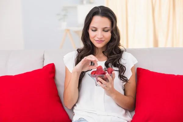 Brunette eating strawberries on couch — Stock Photo, Image