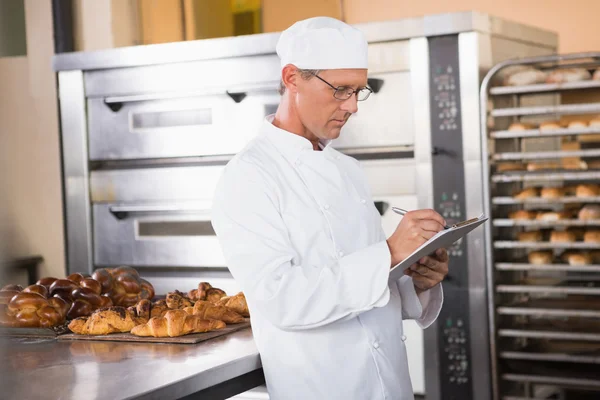 Focused baker writing on clipboard — Stock Photo, Image