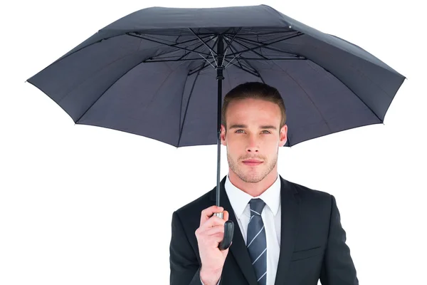 Unsmiling businessman sheltering under umbrella — Stock Photo, Image