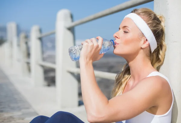 Fit Blondine sitzt auf Seebrücke und trinkt Wasser — Stockfoto