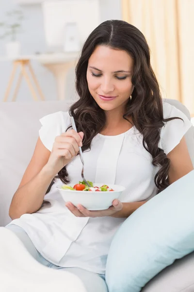 Brunette eating salad on couch — Stock Photo, Image