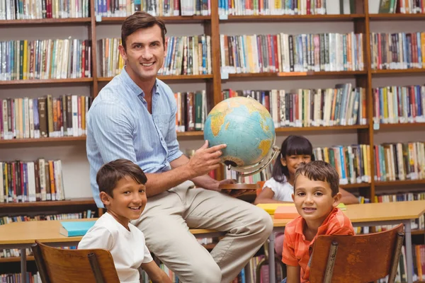 Schattig leerlingen en leraar kijken naar globe in bibliotheek — Stockfoto