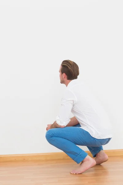 Hombre agachado en el suelo mirando a la pared —  Fotos de Stock