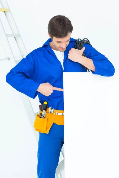 Electrician with wire pointing at bill board — Stock Photo, Image