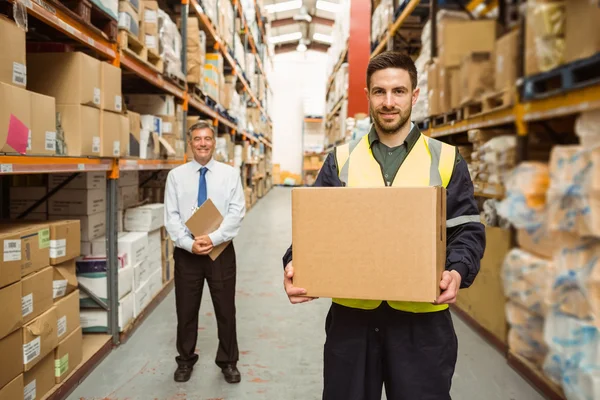 Warehouse worker smiling at camera carrying a box — Stock Photo, Image