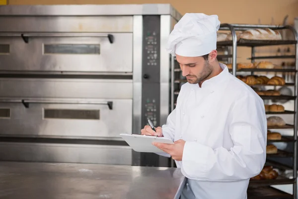 Focused baker writing on clipboard — Stock Photo, Image