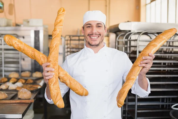 Lachende baker houden drie stokbrood — Stockfoto