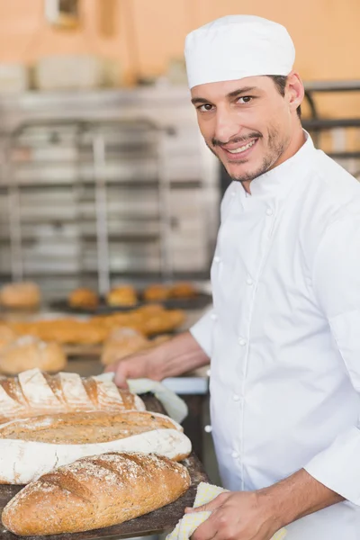 Panadero sonriente sosteniendo bandeja de pan — Foto de Stock