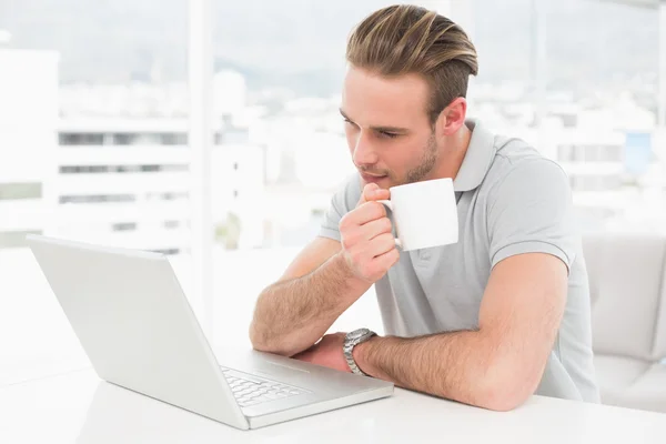 Zakenman holding cup tijdens het gebruik van laptop — Stockfoto