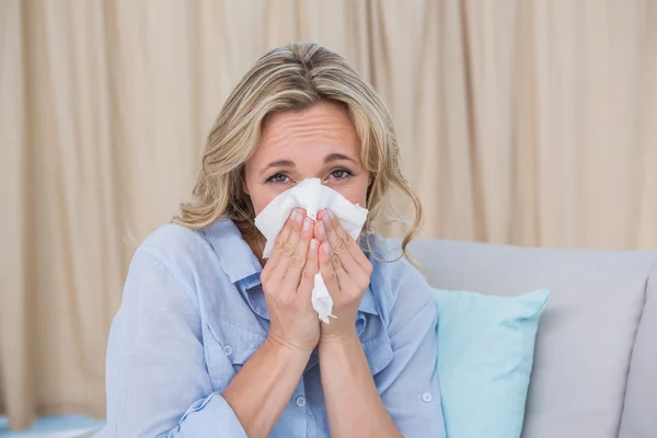 Enferma rubia en el sofá estornudando sobre el tejido —  Fotos de Stock