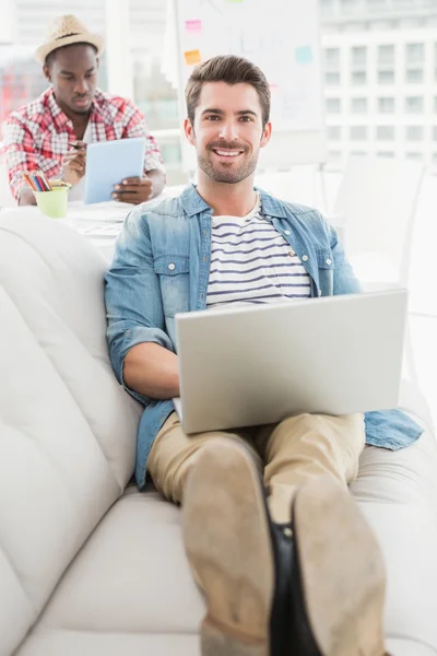 Smiling businessman using laptop on couch — Stock Photo, Image