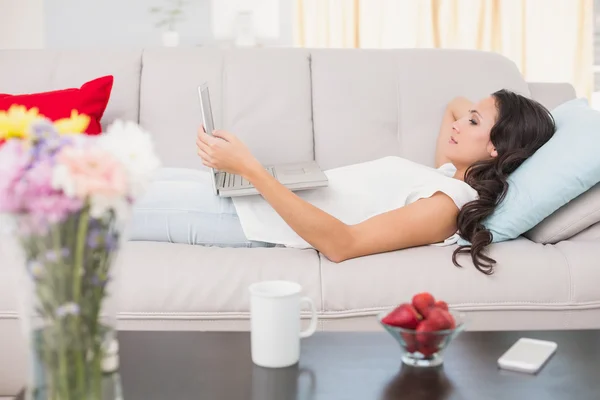 Brunette lying on couch using laptop — Stock Photo, Image
