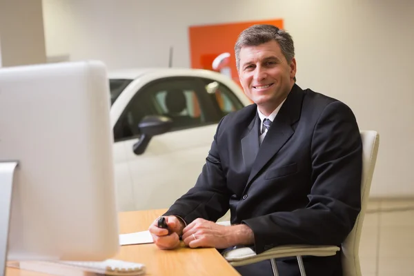 Smiling businessman sitting at his desk holding a car key — Stock Photo, Image