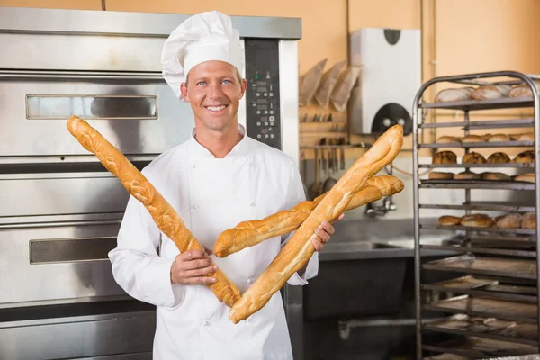 Smiling baker holding three baguettes — Stock Photo, Image