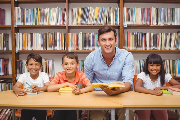 Cute pupils and teacher looking at camera in library — Stock Photo, Image