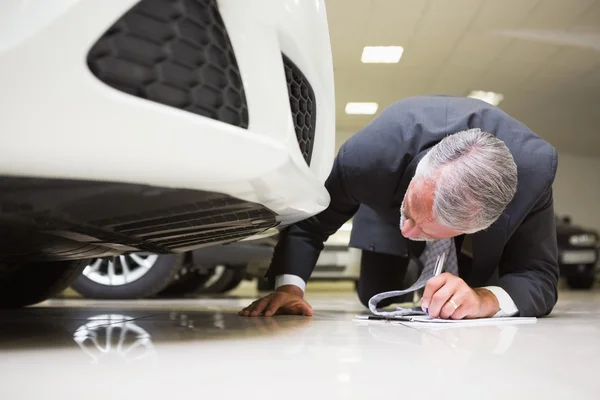 Geschäftsmann schaut beim Schreiben auf Klemmbrett unter das Auto — Stockfoto