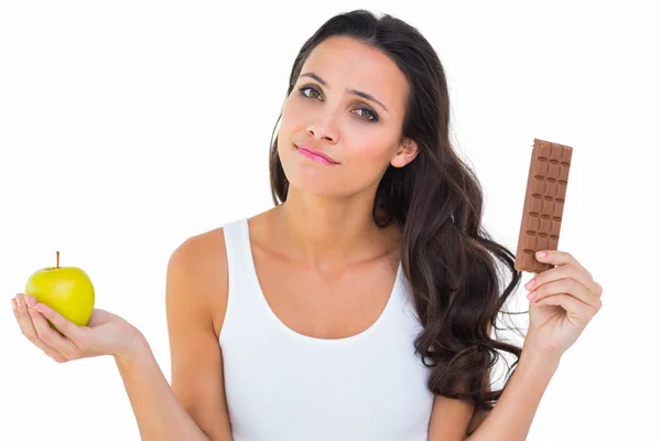 Brunette deciding between apple and chocolate — Stock Photo, Image