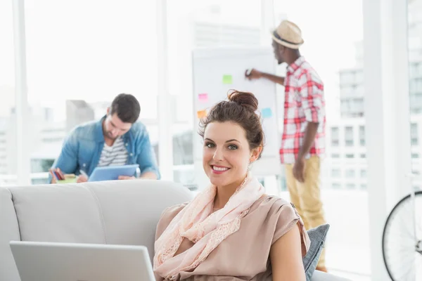 Mujer de negocios sonriente en el sofá utilizando el ordenador portátil —  Fotos de Stock