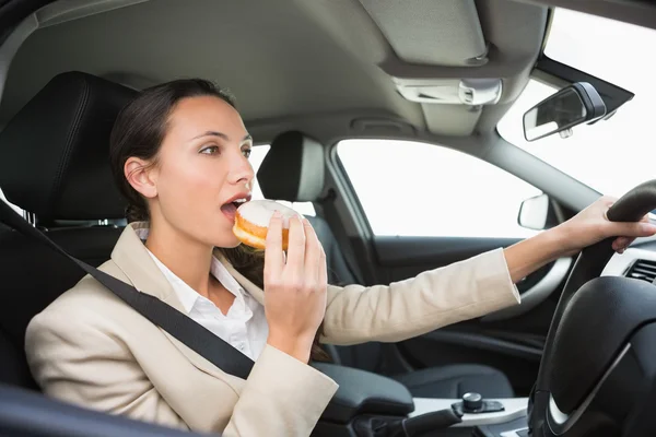 Bonita mulher de negócios tendo donut enquanto dirige — Fotografia de Stock