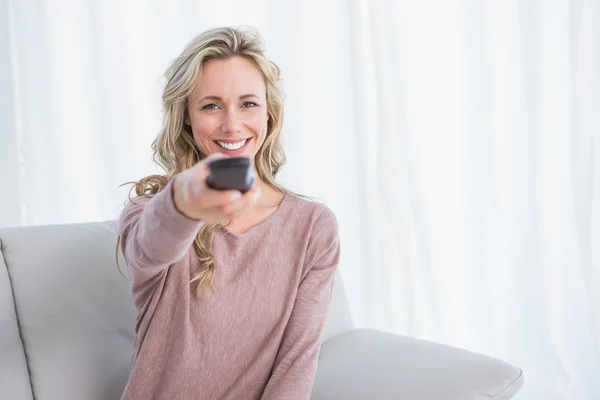 Blonde on couch changing tv channel — Stock Photo, Image