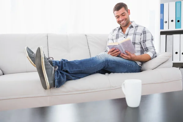 Relaxante homem em um sofá com um livro — Fotografia de Stock