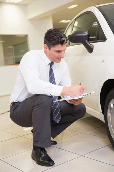 Businessman looking at car while writing on clipboard — Stock Photo, Image