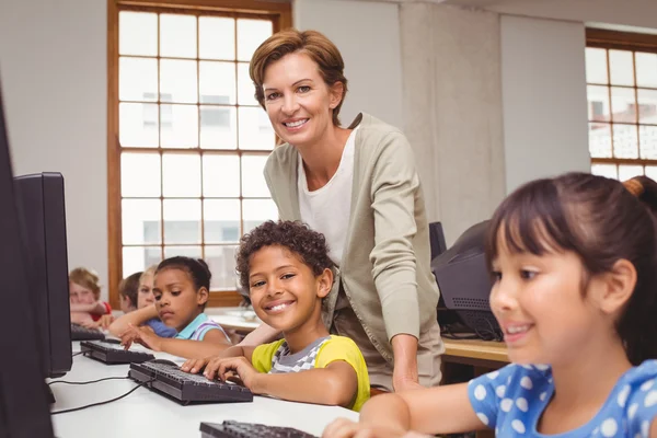 Lindo alumno en clase de informática con el profesor sonriendo a la cámara — Foto de Stock