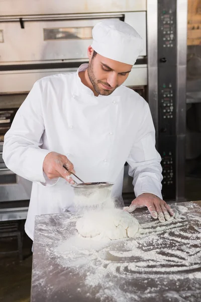 Baker sieving flour on the dough — Stock Photo, Image
