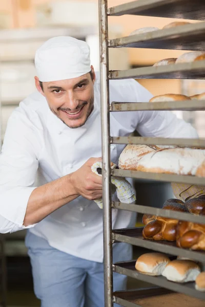 Smiling baker pushing tray of bread — Stock Photo, Image