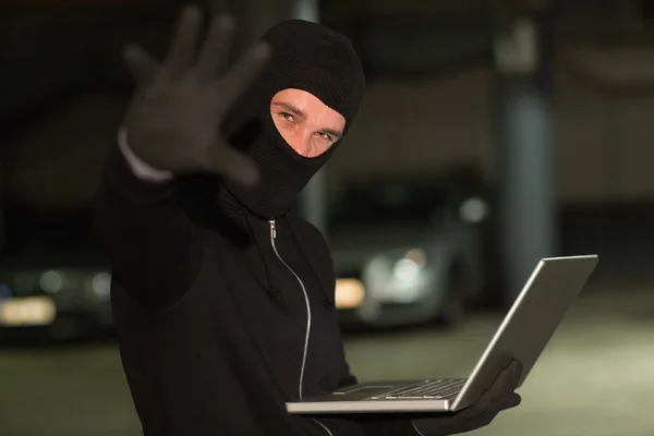 Hacker mit Sturmhaube gestikuliert und benutzt Laptop — Stockfoto