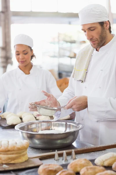 Baker peneirando farinha em uma tigela — Fotografia de Stock