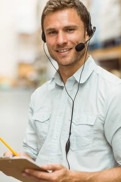 Warehouse manager dragen hoofdtelefoon schrijven op Klembord — Stockfoto