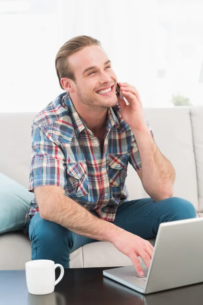 Χαμογελαστός άνθρωπος σε ένα τηλέφωνο με ένα φορητό υπολογιστή στο σπίτι — Φωτογραφία Αρχείου