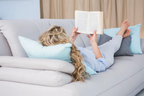 Bionda sdraiata sul divano lettura libro — Foto Stock