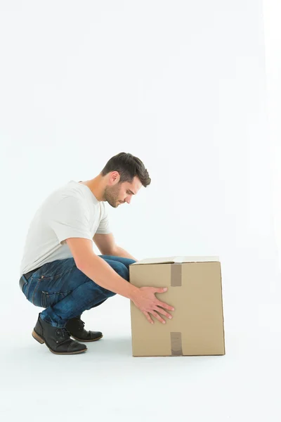 Delivery man crouching while picking cardboard box — Stock Photo, Image