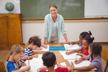 Teacher and pupils working at desk together clipart