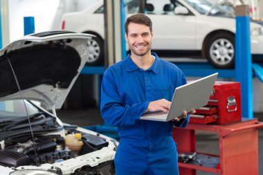 Smiling mechanic using his laptop clipart