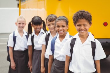 Cute schoolchildren smiling at camera by the school bus clipart