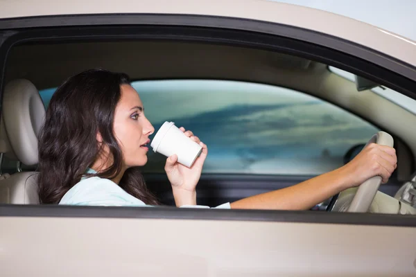 Улыбающаяся женщина за рулем машины, когда пьет кофе — стоковое фото