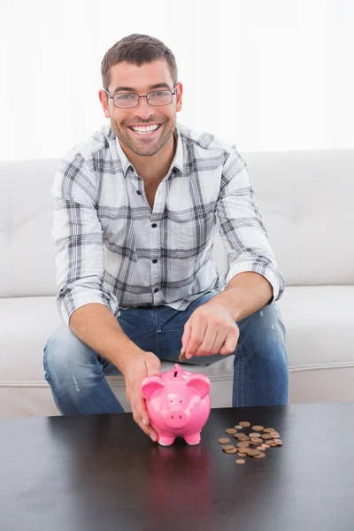 Sorrindo homem colocando moedas em um banco porquinho — Fotografia de Stock